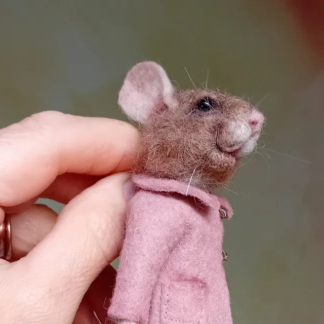 a hand holding a tiny mouse in a pink coat