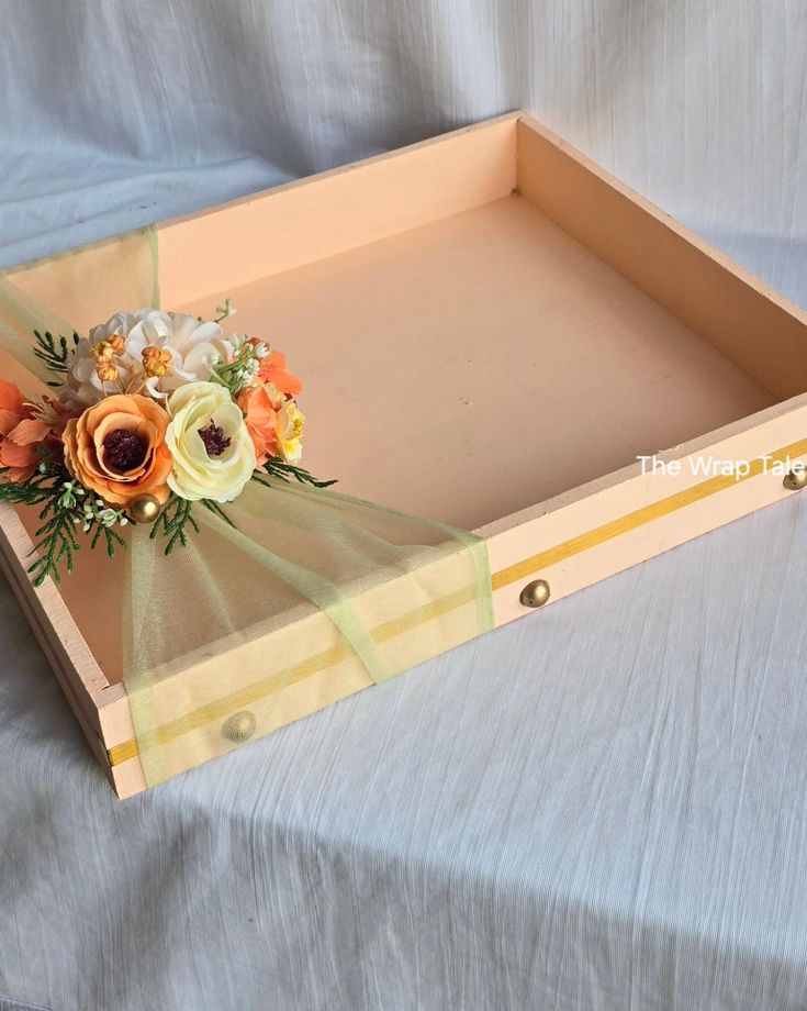 an empty wooden box with flowers and ribbons on it's sides, sitting on a white sheet