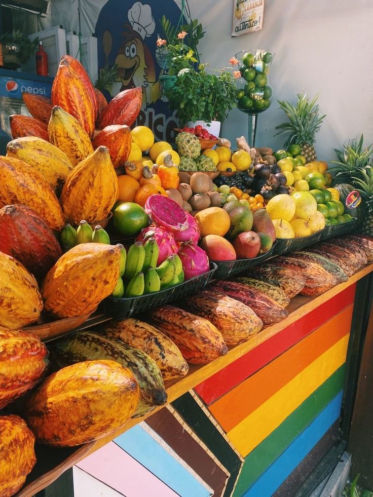 an assortment of tropical fruits on display at a market stall with rainbow colors and flowers