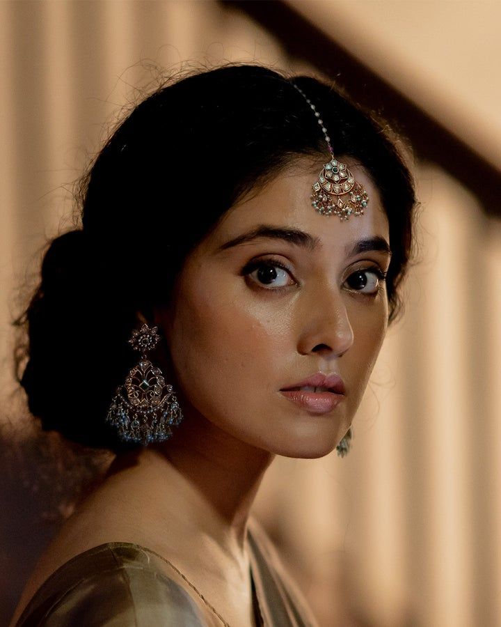 a woman with dark hair and earrings on her head looking off into the distance while standing in front of a staircase