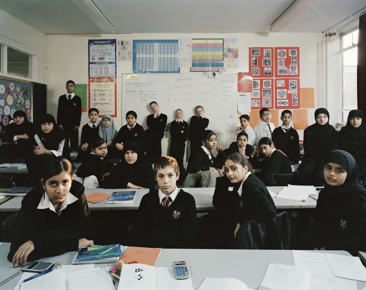 a group of students sitting at desks in a classroom with their teacher standing behind them