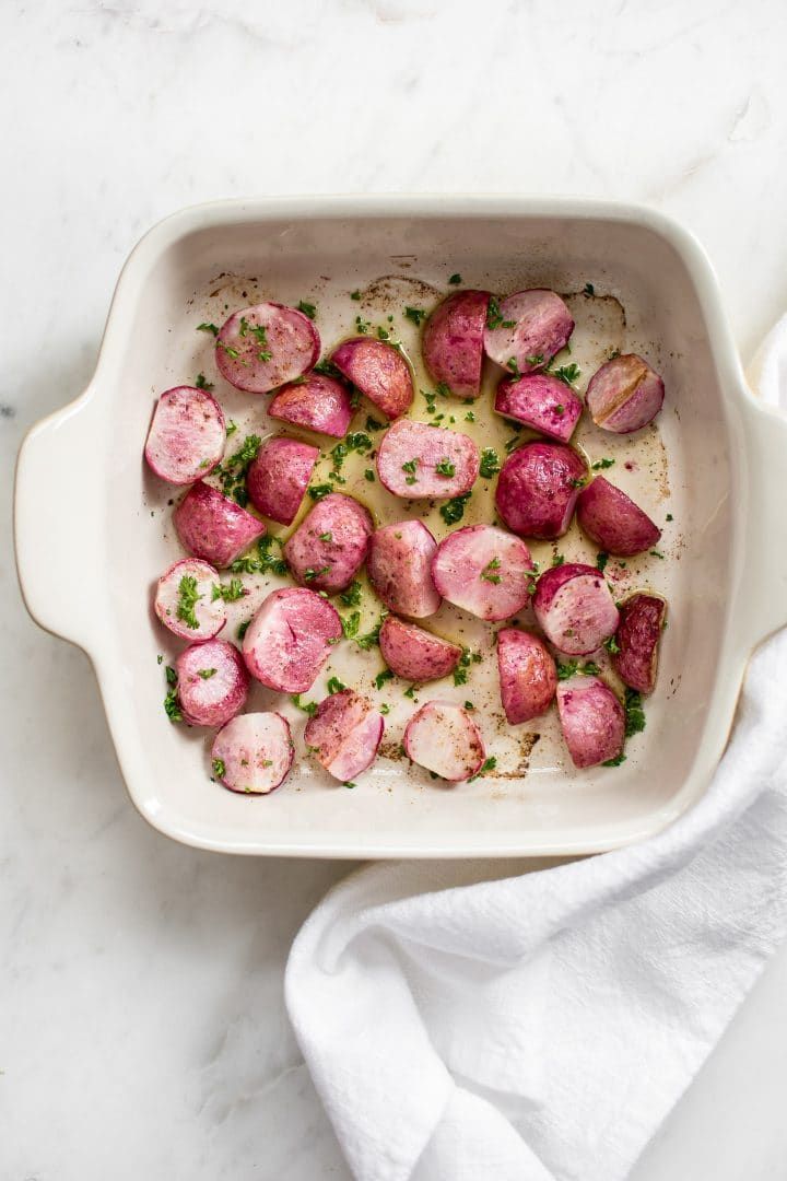 a white casserole dish filled with potatoes and parsley on a marble surface