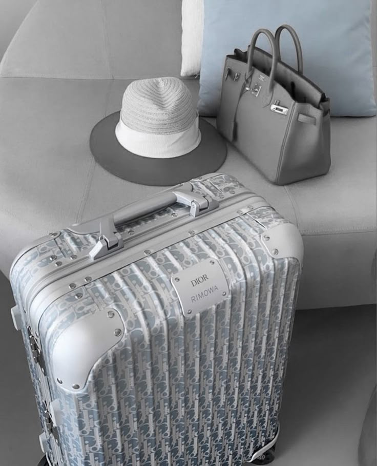 two pieces of luggage sitting next to each other on a couch with a hat and purse