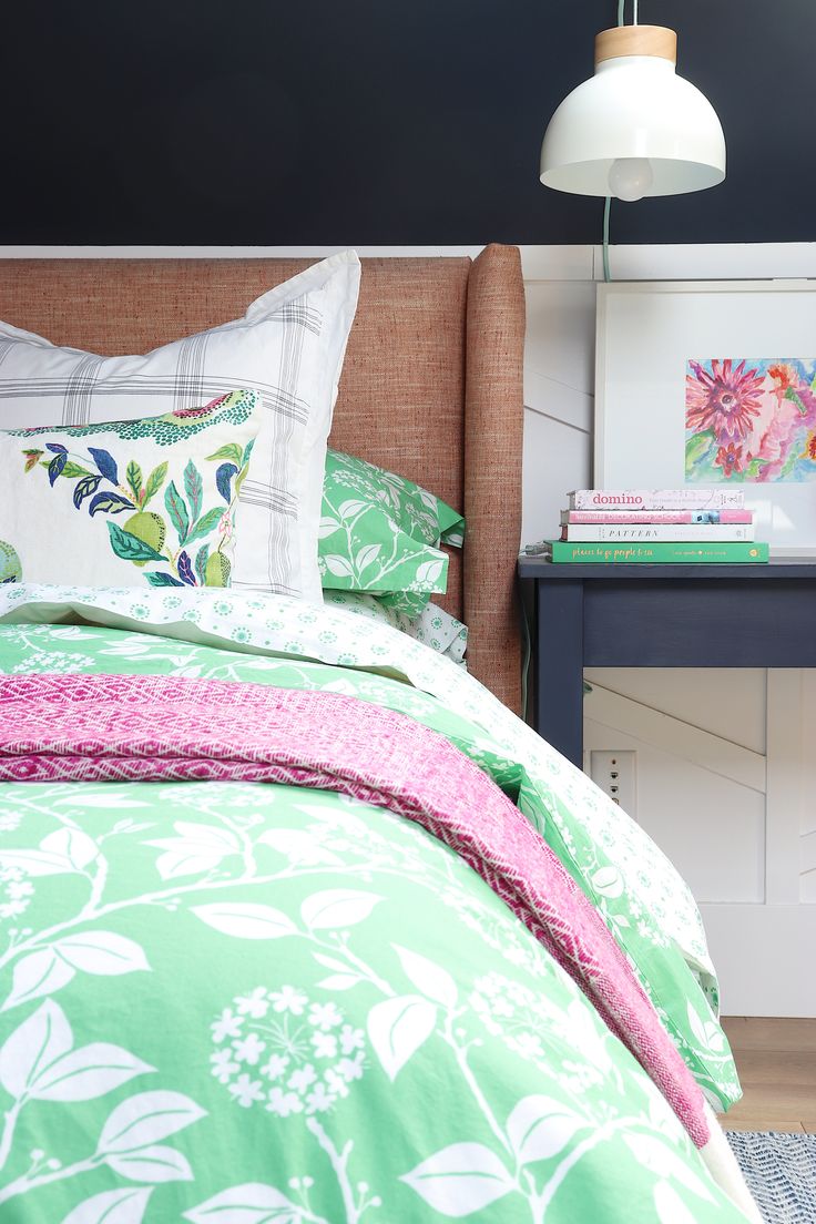 a bed with green and pink comforter next to a night stand