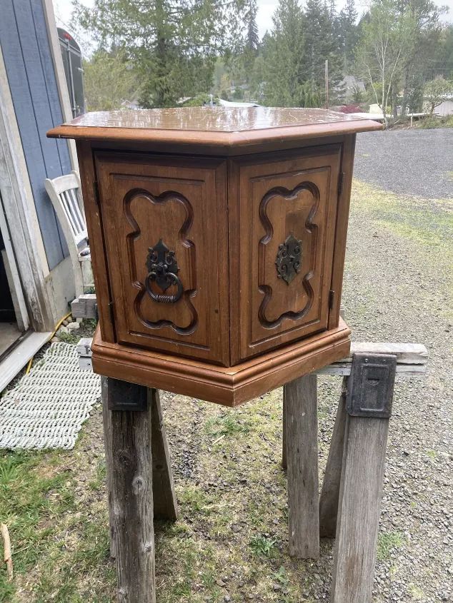 an old wooden cabinet sitting on top of two wood posts in the grass next to a building