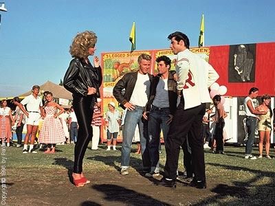 two men and one woman standing in front of a carnival tent with people looking at them