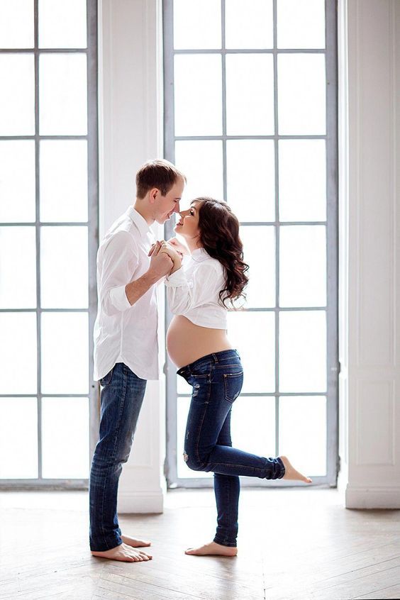 a pregnant woman standing next to a man in front of a window while holding her belly