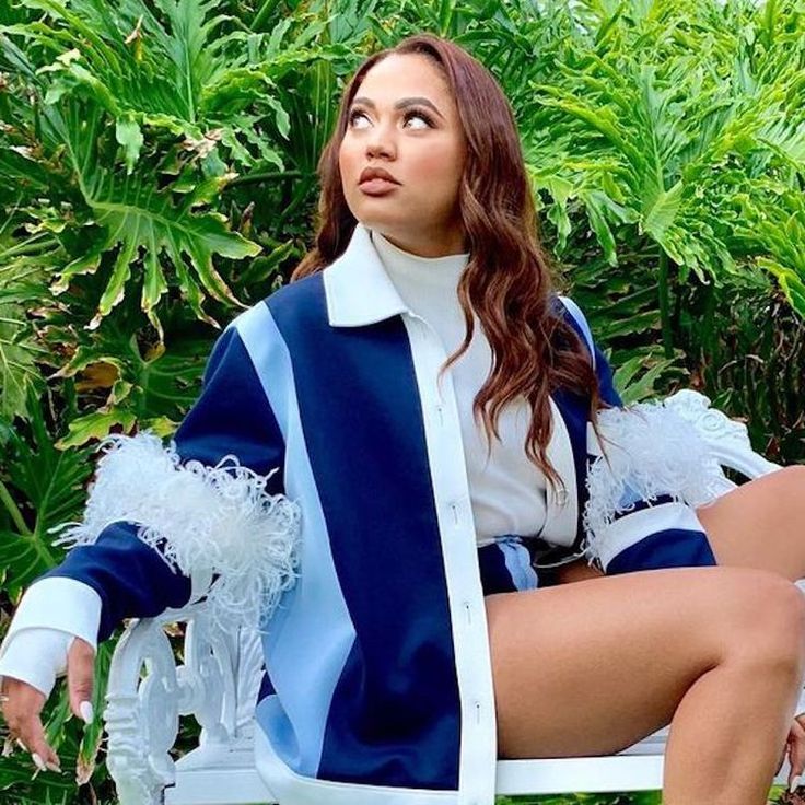 a woman sitting on top of a white bench in front of some grass and bushes