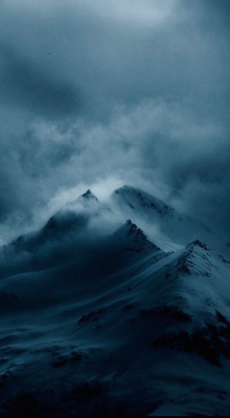 a large mountain covered in snow under a cloudy sky with dark clouds above it,