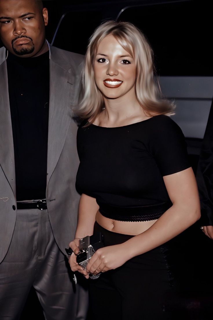 a woman standing next to a man in a gray suit and black top with blonde hair