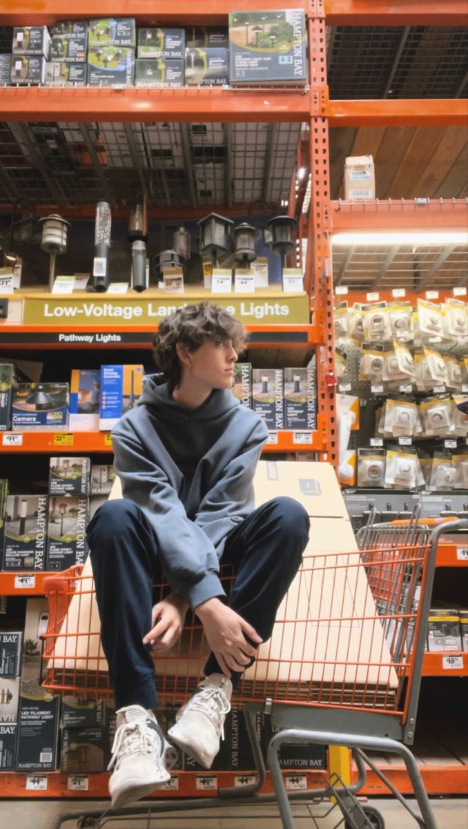 a man sitting on top of a shopping cart in a grocery store next to shelves