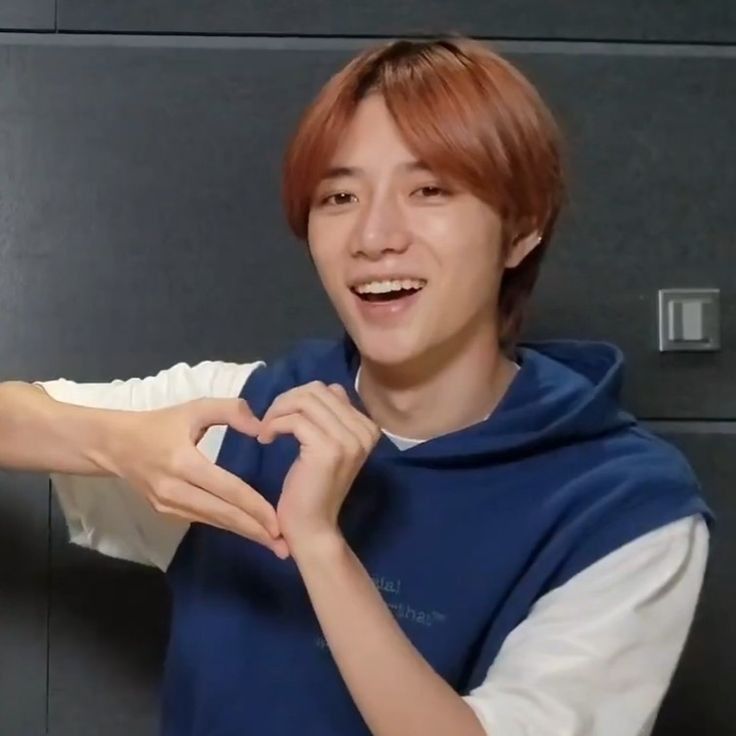 a young man making a heart with his hands while standing in front of a wall