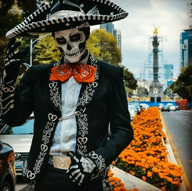 a skeleton wearing a sombrero and bow tie standing in front of orange flowers