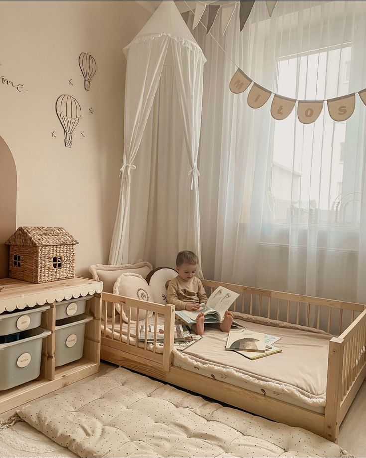 a little boy sitting in his crib reading a book while looking out the window