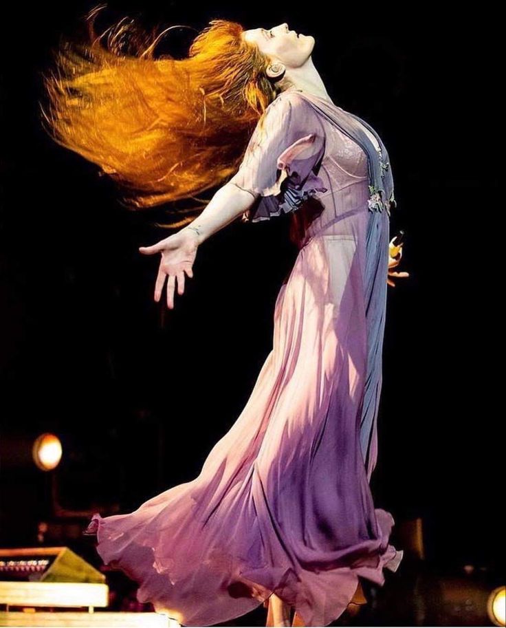 a woman in a long dress is dancing on stage with her hair blowing in the wind