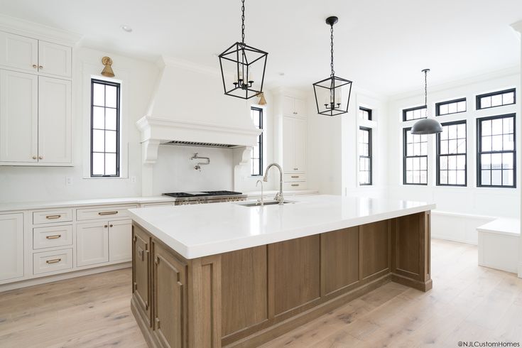 a large kitchen with white cabinets and wooden floors, two pendant lights hanging over the island