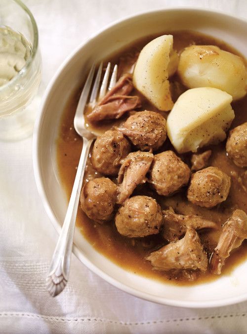 a bowl filled with meat, potatoes and gravy next to a glass of water