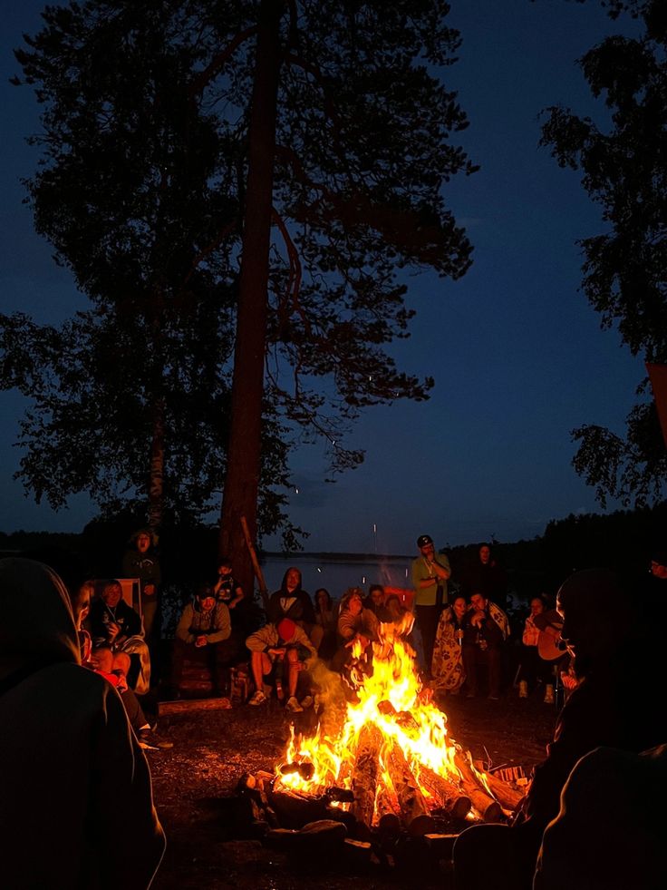 people sitting around a campfire at night with their backs turned to the camera,