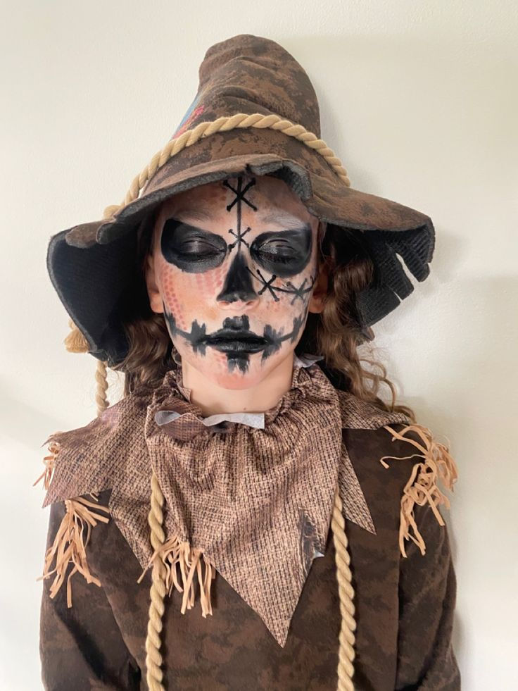 a woman with makeup and face paint is wearing a scarecrow hat, brown shirt and braids