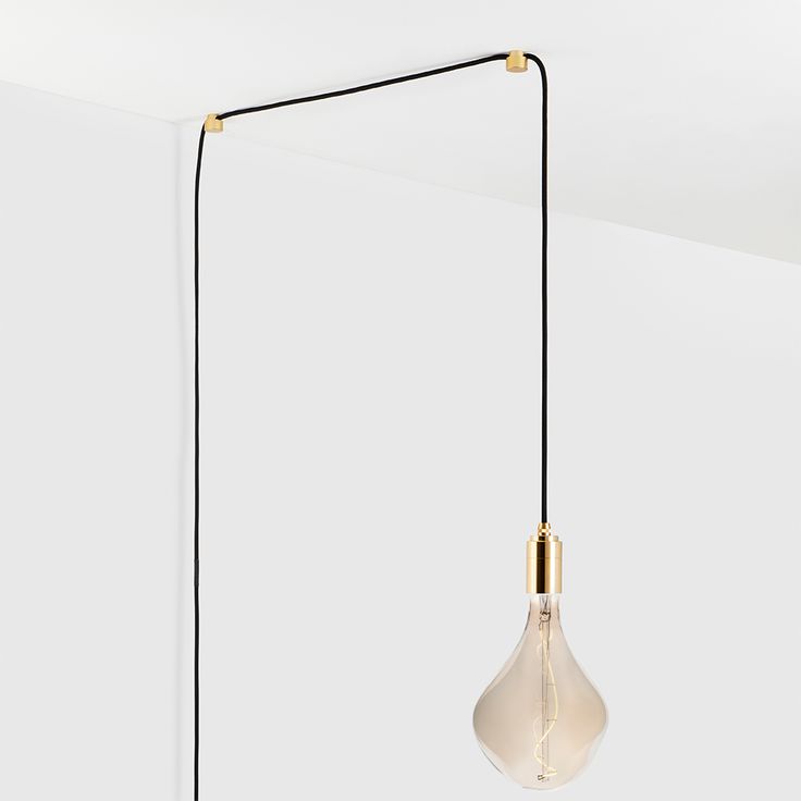 a light bulb hanging from a black cord with a white wall in the back ground