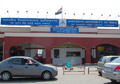 two cars parked in front of an airport authority of india building with flags on top