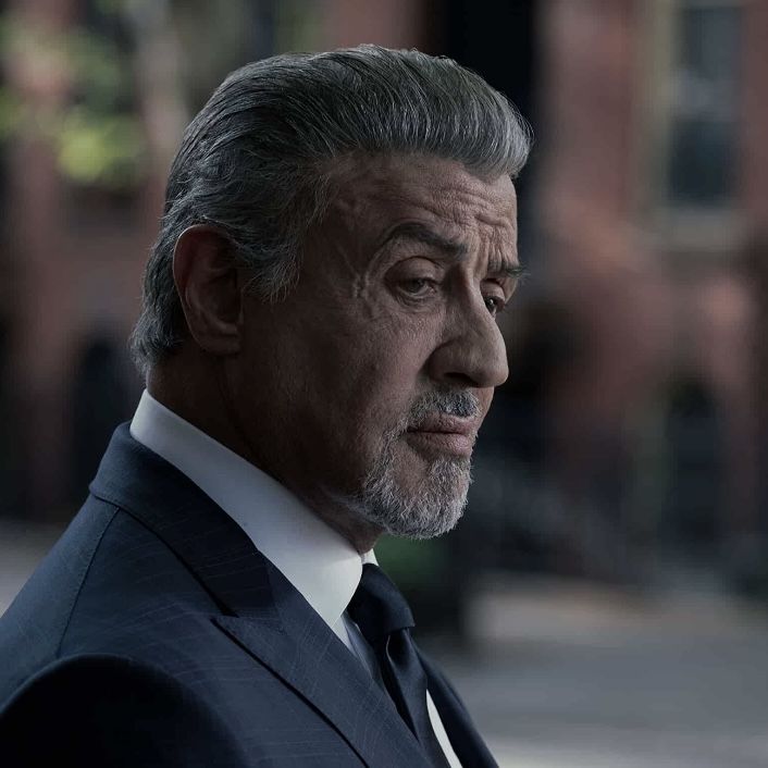 an older man in a suit and tie looking off into the distance while standing on a city street