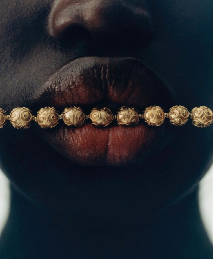 a woman's face with gold beads on her lip and nose chain in front of her mouth