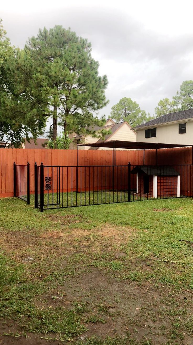 a fenced in yard with a dog house behind it and trees on the other side