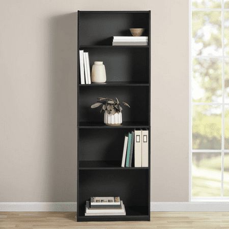 a black book shelf with books on it in front of a white wall and wooden floor