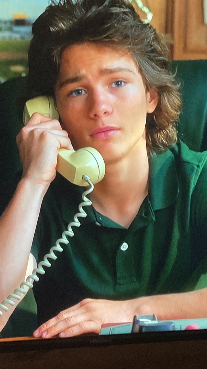 a young man sitting at a table talking on the phone