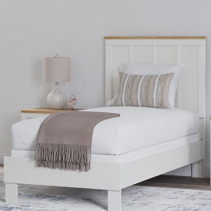 a white bed sitting on top of a wooden floor next to a nightstand with a lamp