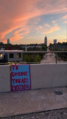 a sign that says to someone you are everything on the side of a bridge with buildings in the background