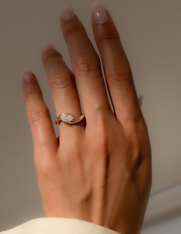 a woman's hand wearing a gold ring with a diamond in the middle and a leaf on it