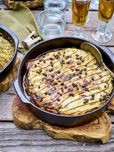 two pans filled with food sitting on top of a wooden table next to glasses