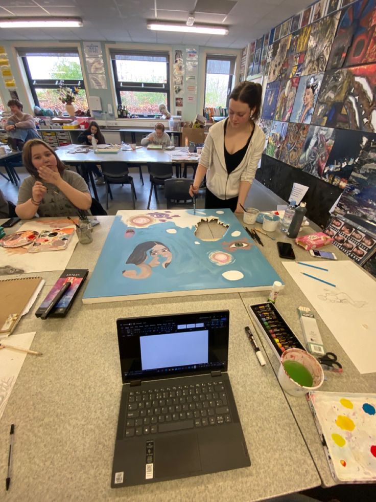 two women sitting at a table with laptops and paintings on the wall behind them