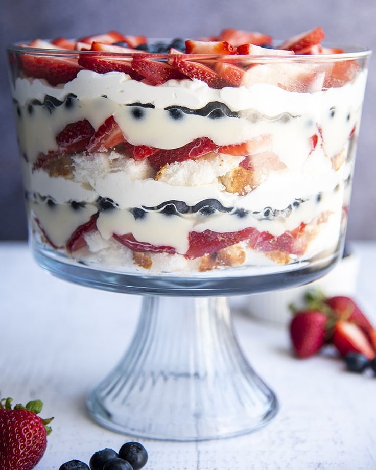 a trifle with strawberries and blueberries in it on a glass cake stand