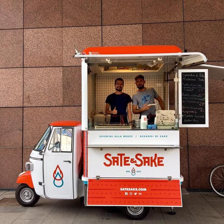 two men standing behind an orange and white food truck