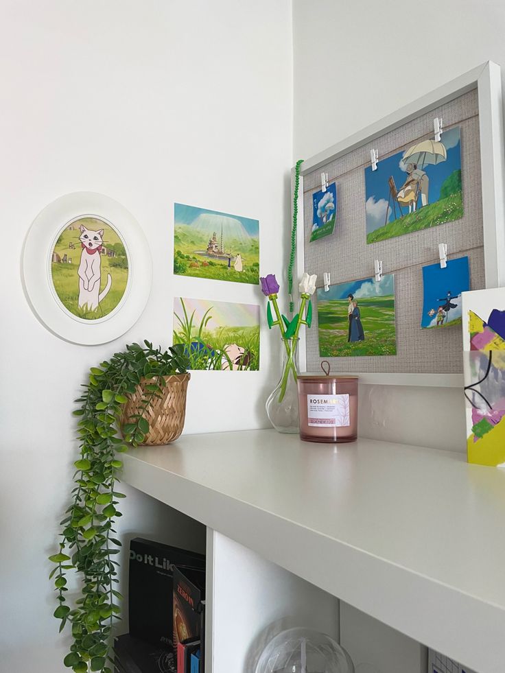 a white shelf topped with pictures and plants next to a plant potted on top of it