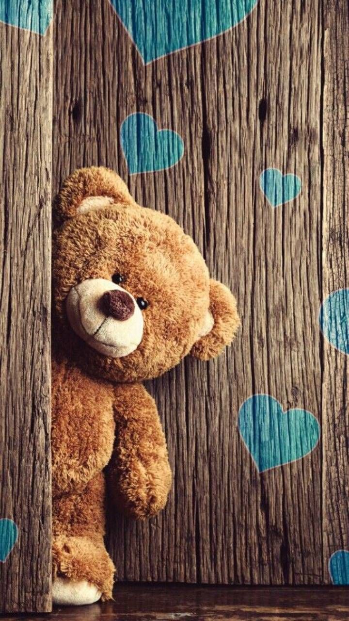 a brown teddy bear sitting on top of a wooden wall with hearts painted on it