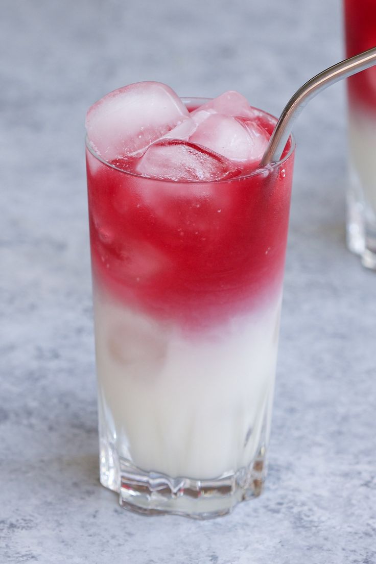 two glasses filled with red and white drinks on top of a gray table next to each other