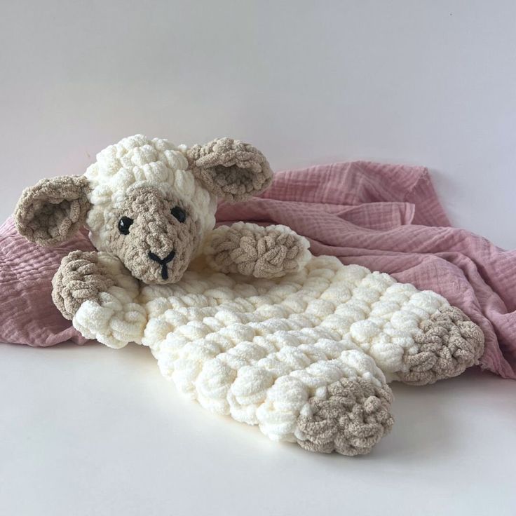 a stuffed sheep laying on top of a pink blanket