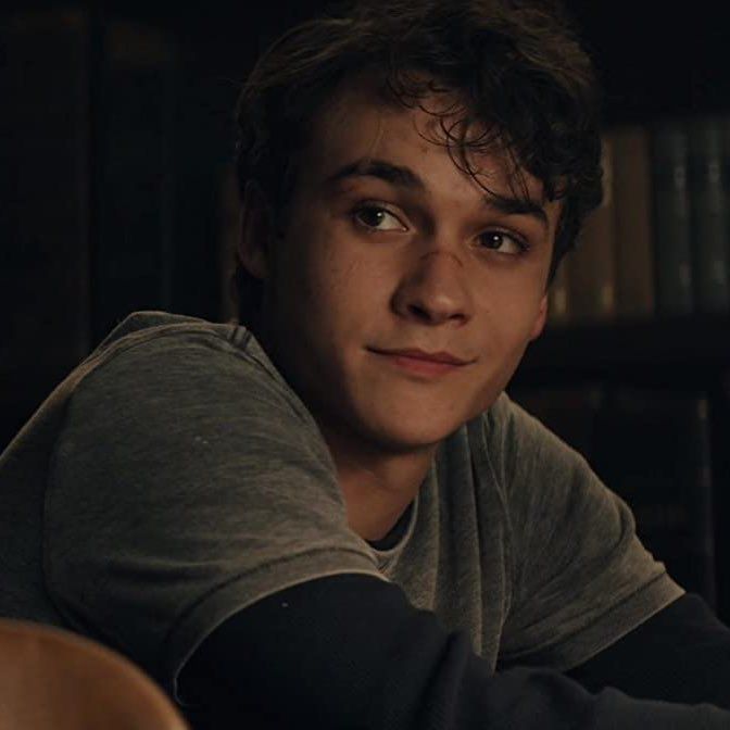 a young man sitting in front of a book shelf