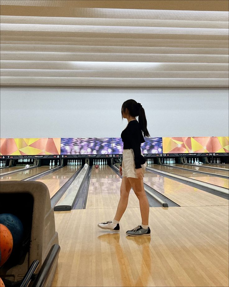 a woman standing on top of a bowling alley next to lanes filled with bowling balls