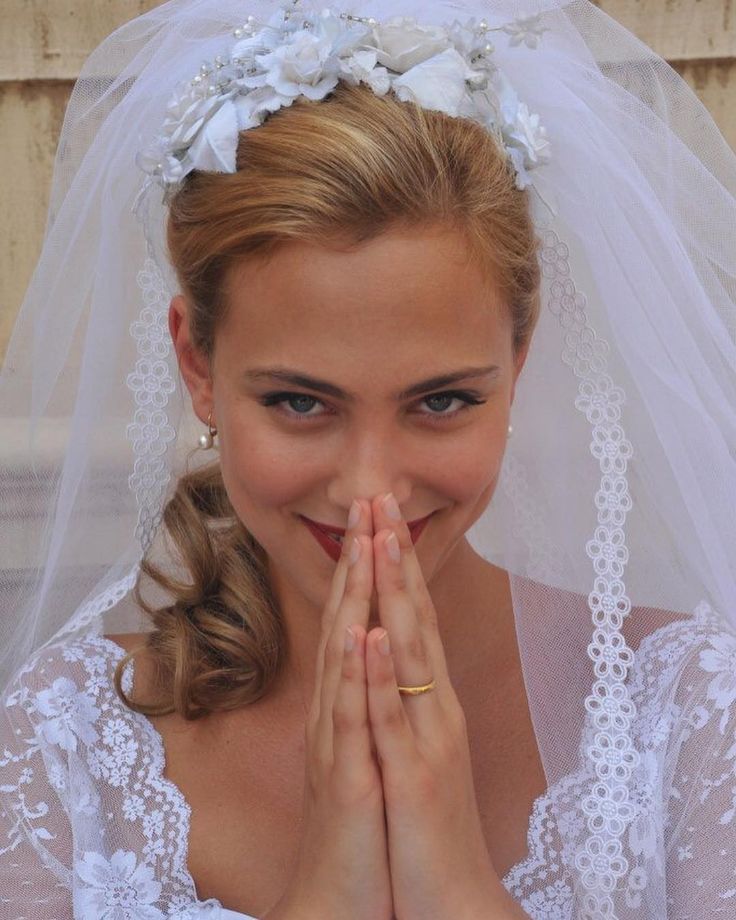 a woman wearing a wedding veil and holding her hands to her face with both hands