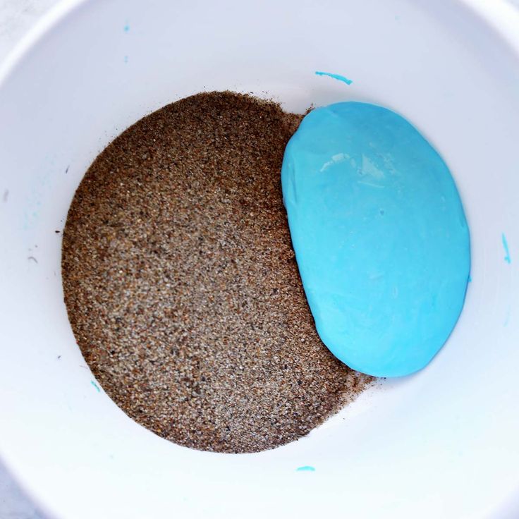 a bowl filled with blue and brown sand next to a white container on top of a table