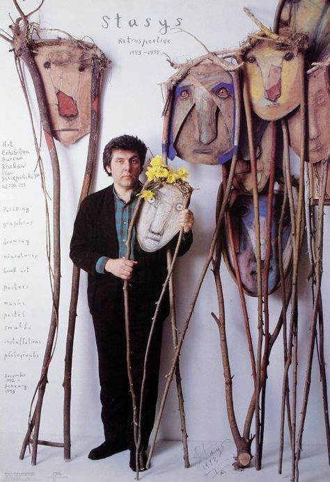 a man holding a vase with flowers in it next to some branches and masks on the wall