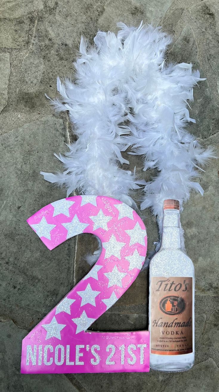 a pink and white number two sign next to a bottle of alcohol with feathers on it