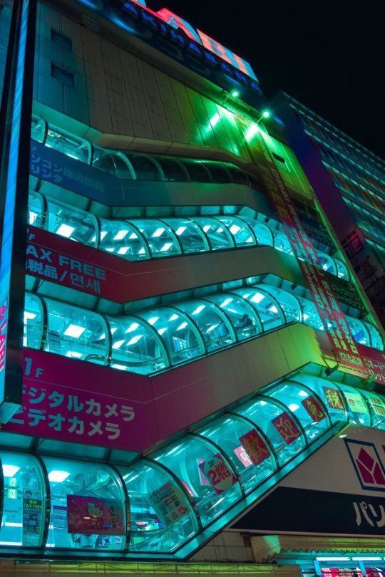 a tall building with neon lights on it's sides and windows at night time