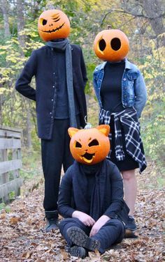 three people wearing pumpkin heads standing next to each other in the leaves with one person sitting on the ground