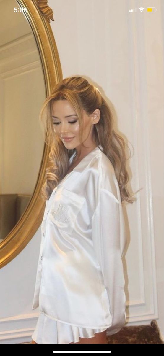 a woman standing in front of a mirror wearing a white shirt and brown skirt with long hair